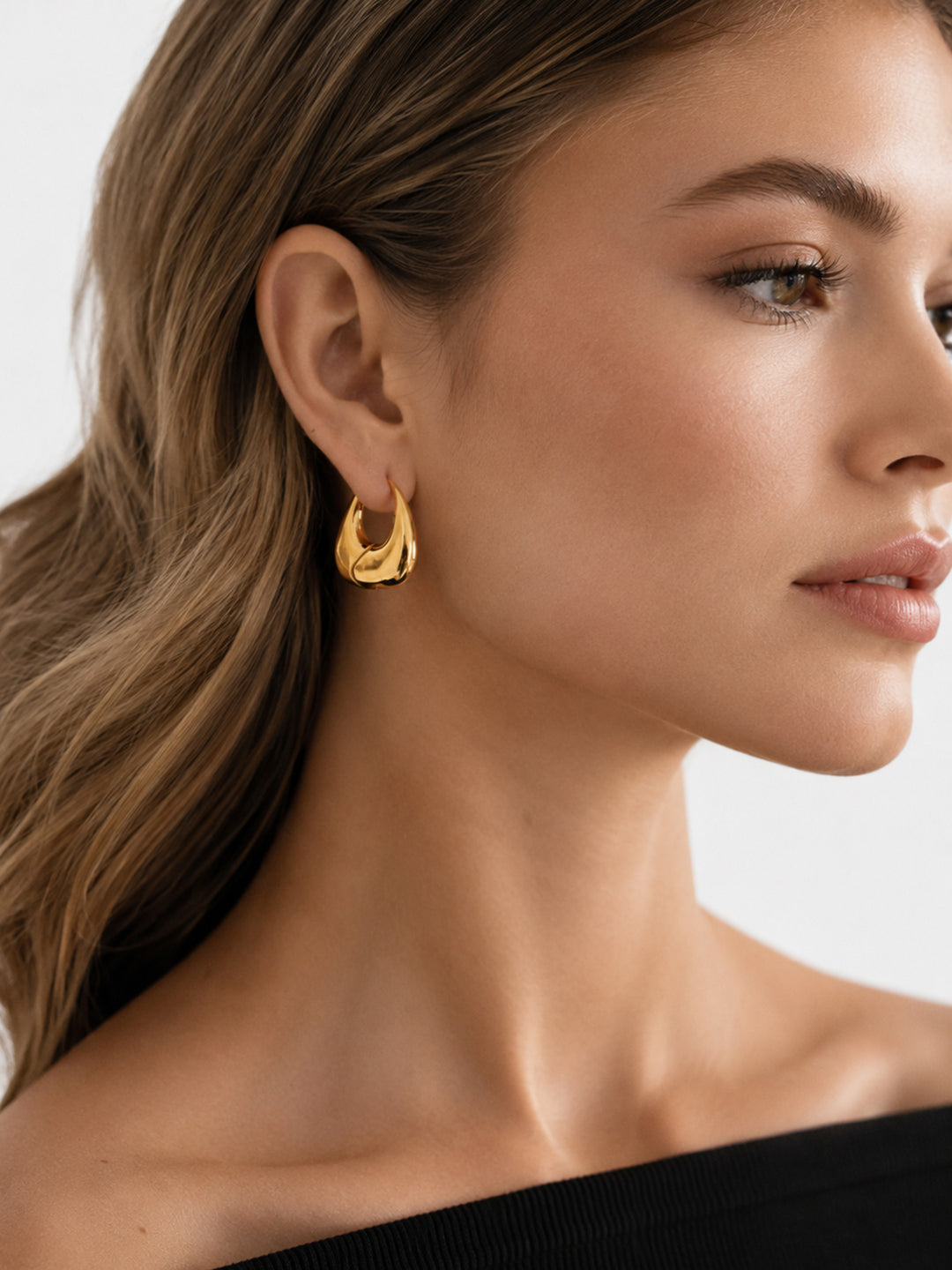 Gold-plated sculptural hoop earrings worn close to the ear