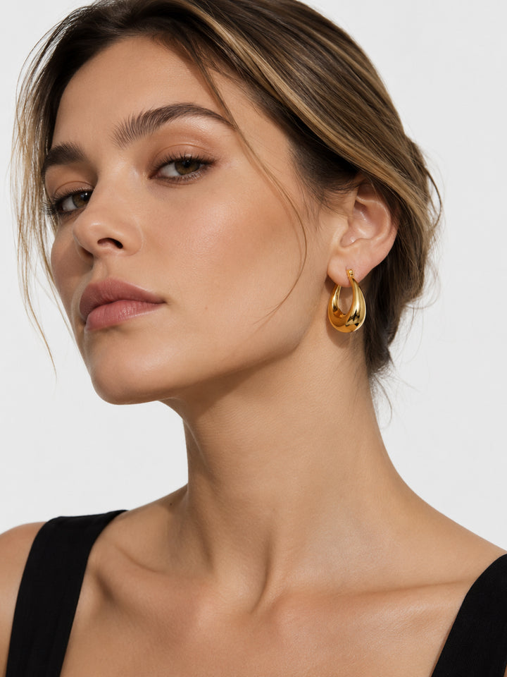 Gold-plated sculptural hoop earrings worn close to the ear