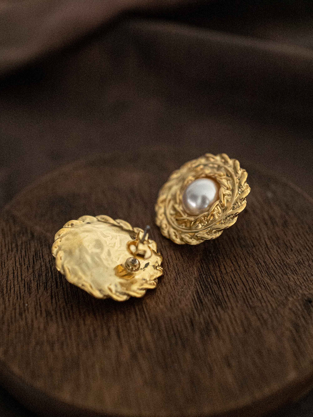 A round gold earring with a pearl in the center.