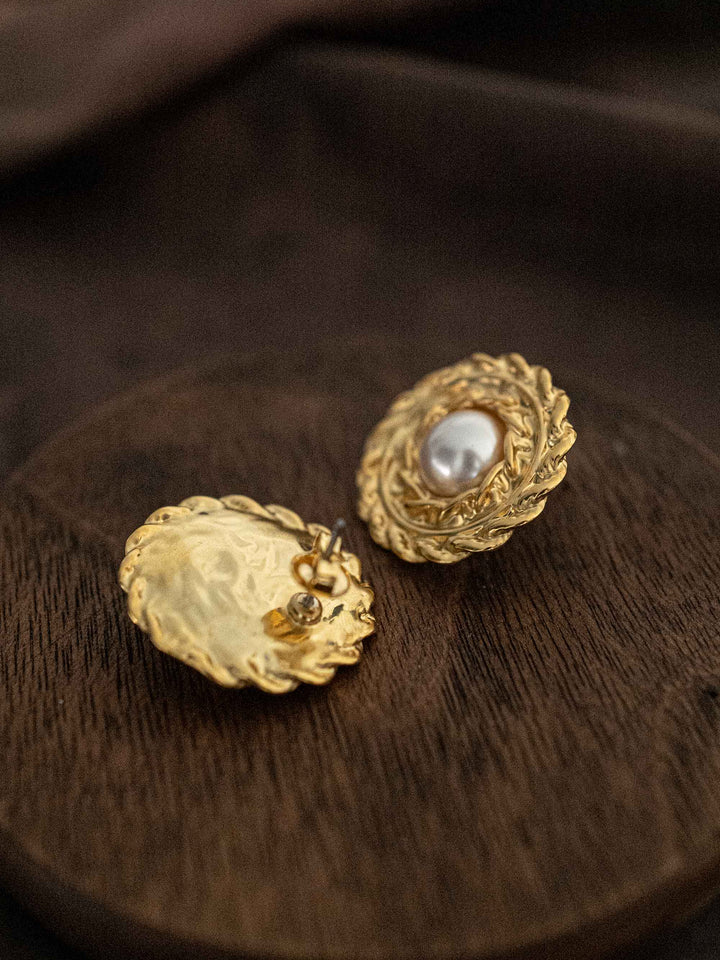 A round gold earring with a pearl in the center.