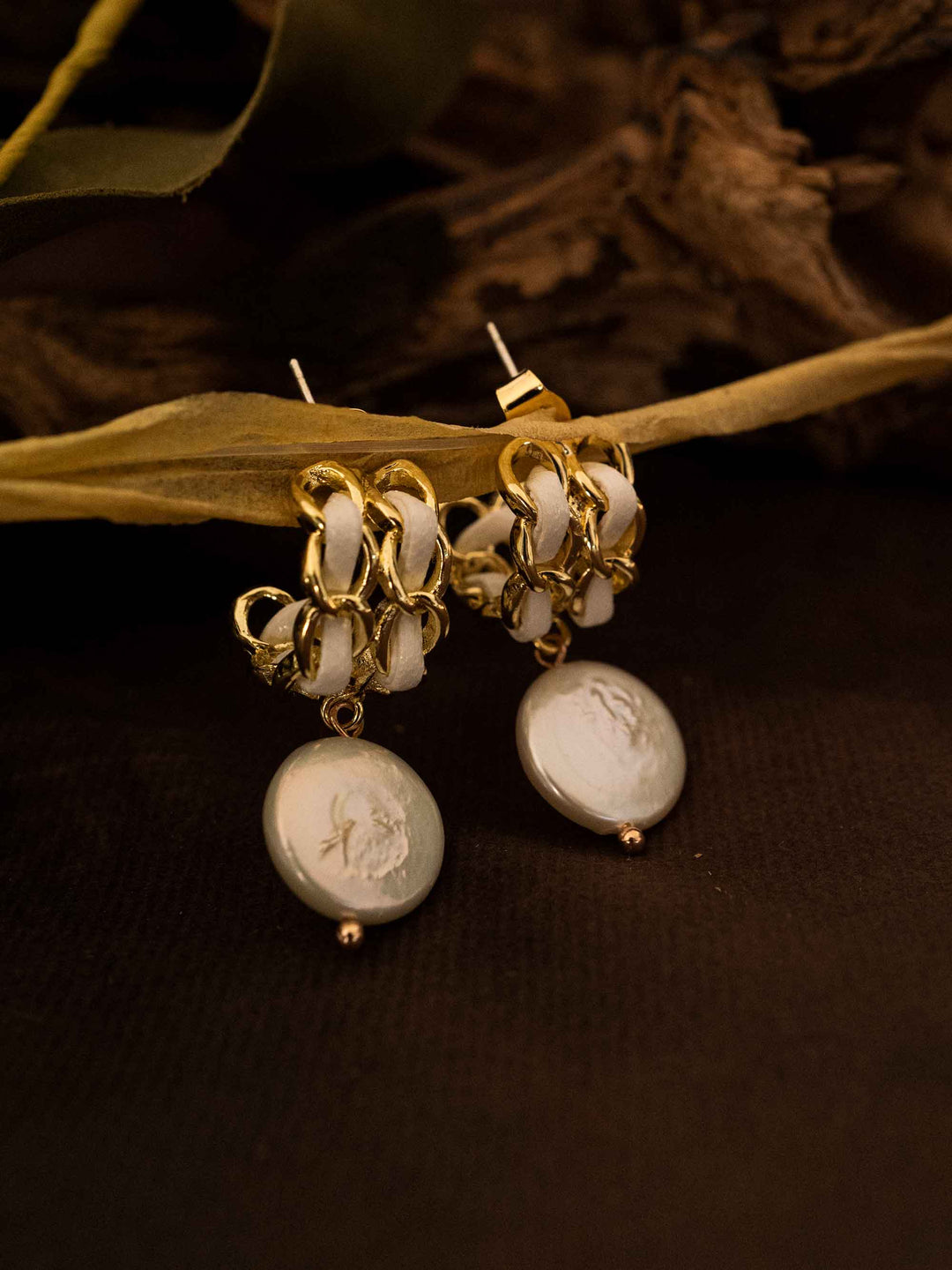 A pair of baroque pearl gold earrings with white ribbon on a grid