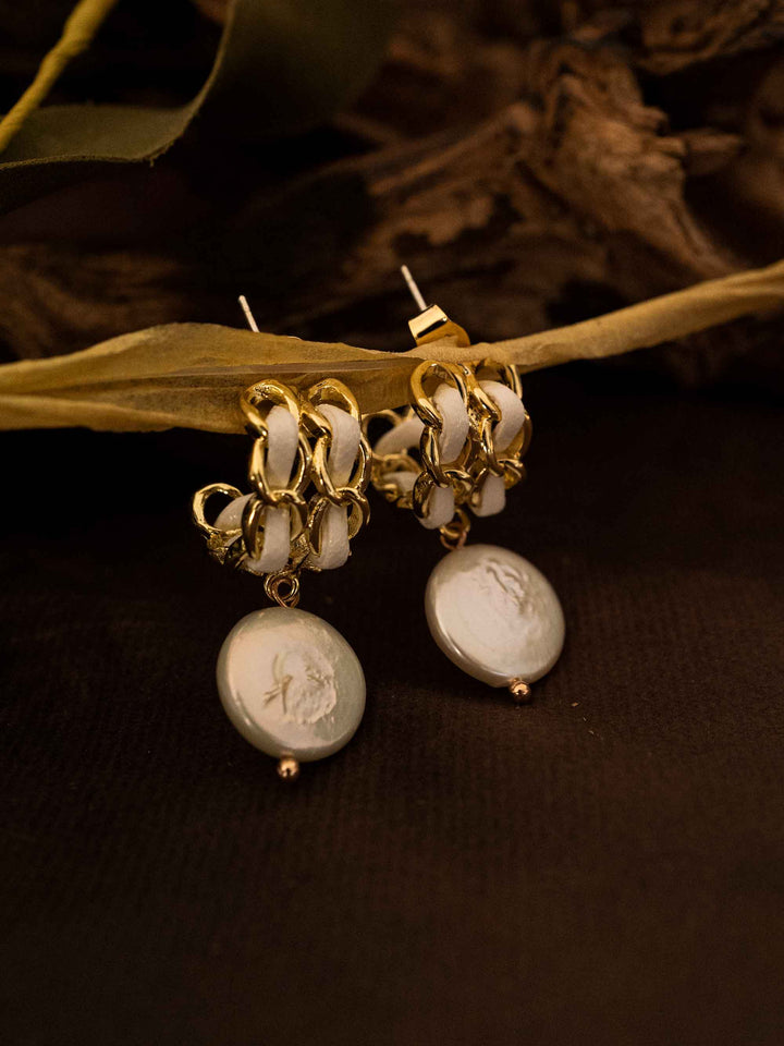 A pair of baroque pearl gold earrings with white ribbon on a grid