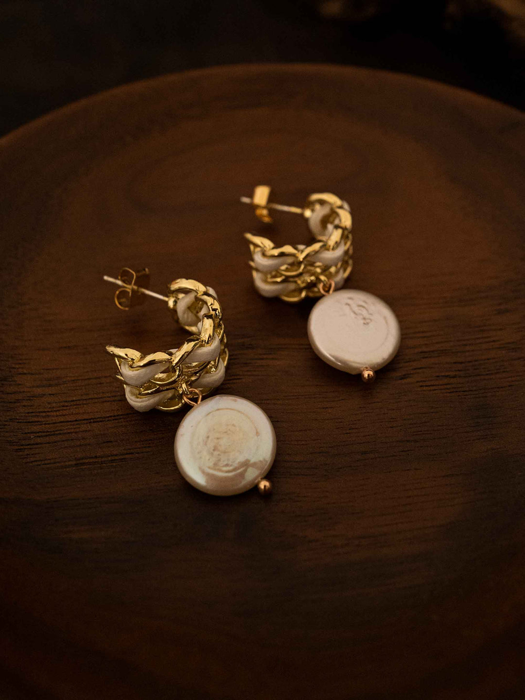 A pair of baroque pearl gold earrings with white ribbon on a grid