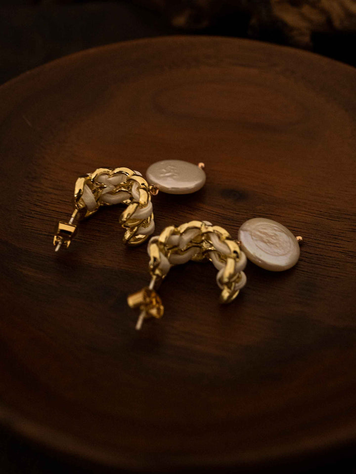 A pair of baroque pearl gold earrings with white ribbon on a grid