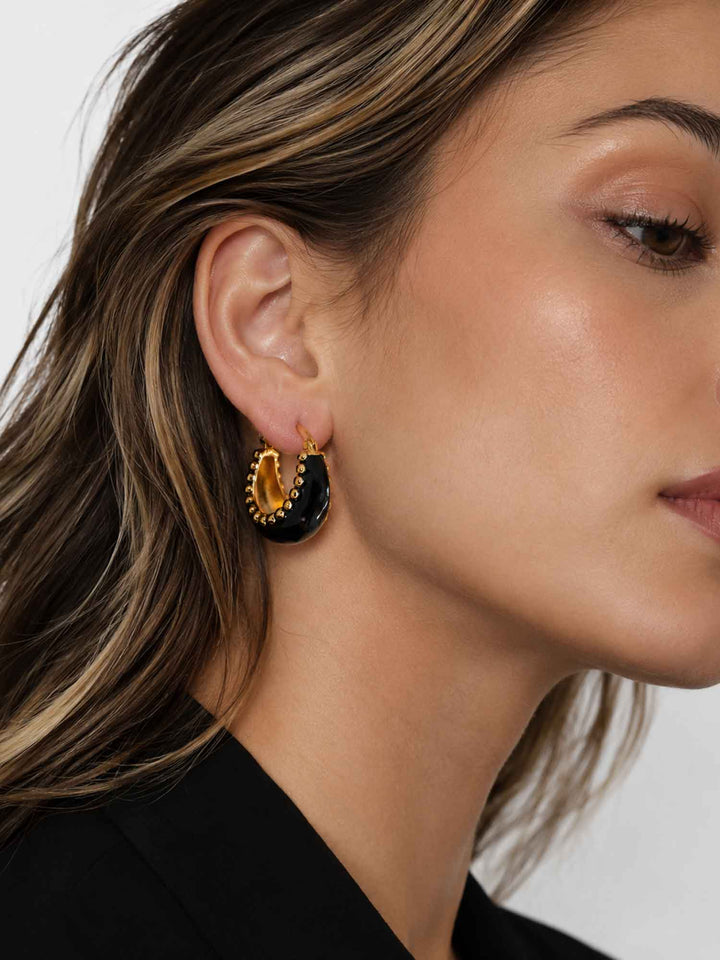 Close-up view of model wearing Brina black and gold hoop earrings