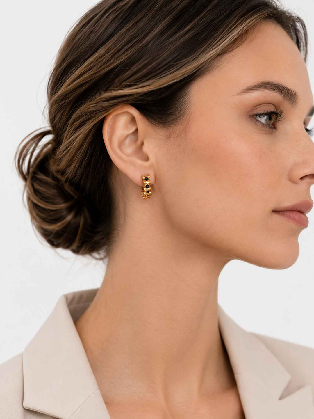 Model wearing Eudora black onyx gold huggie hoop earrings with white blazer