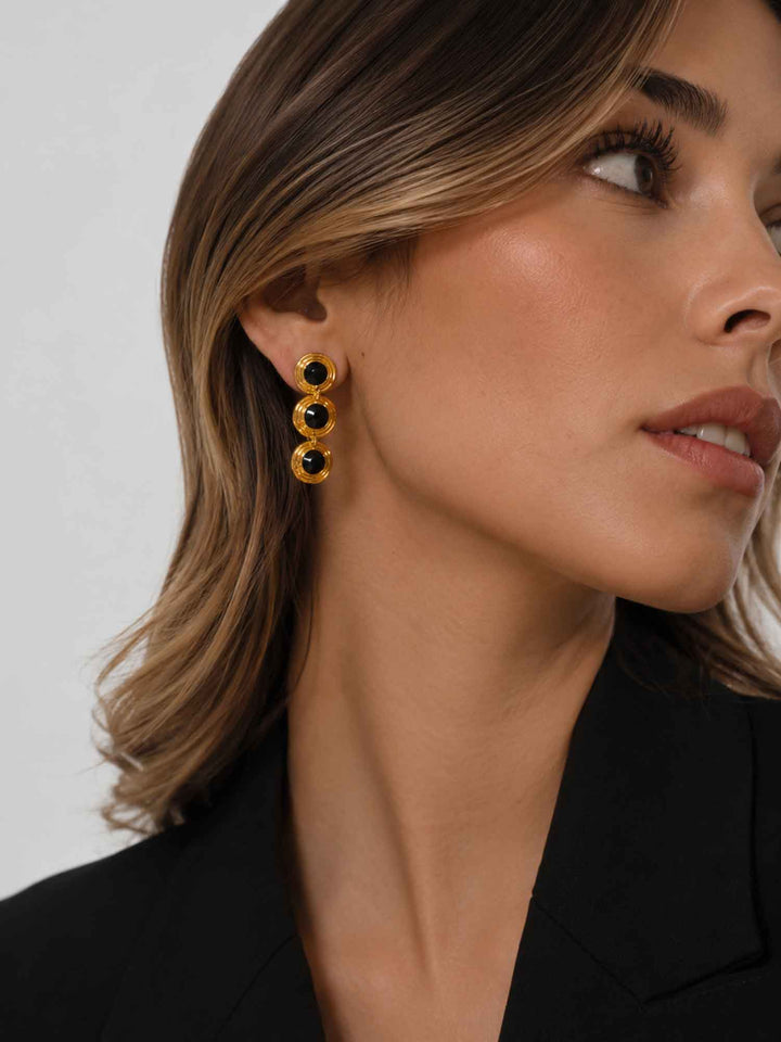 Side view of model wearing Evienne black crystal gold drop earrings with black outfit