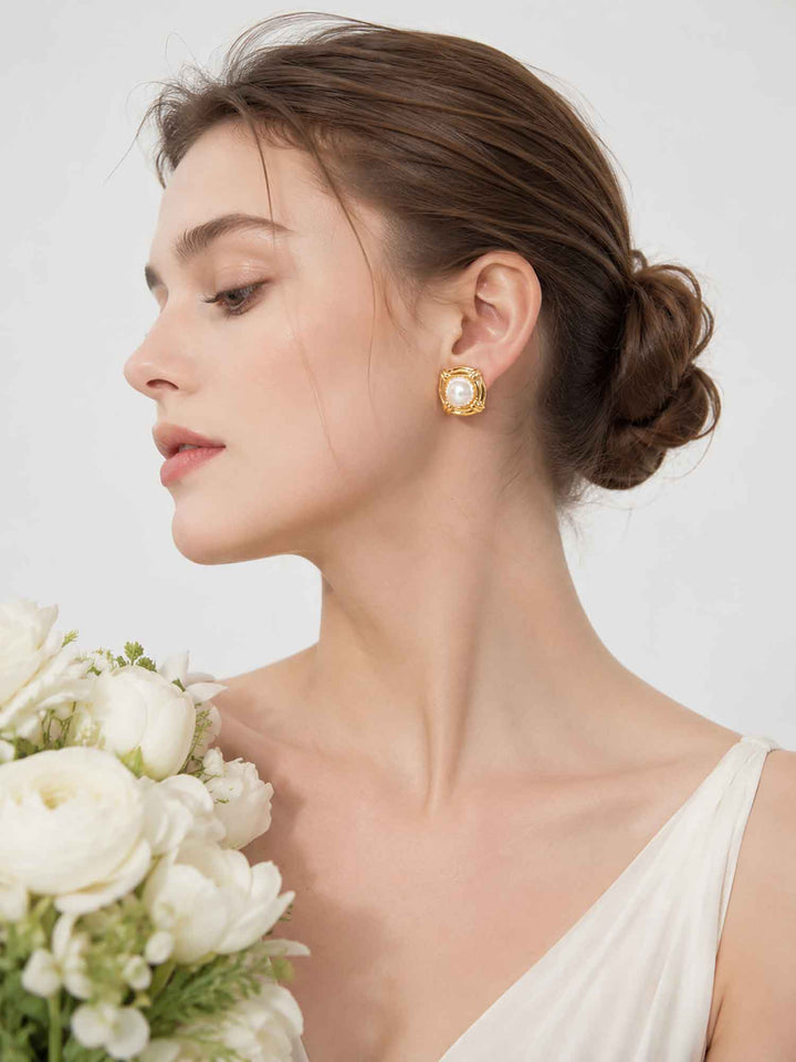 Model wearing gold pearl stud earrings with a bridal bouquet
