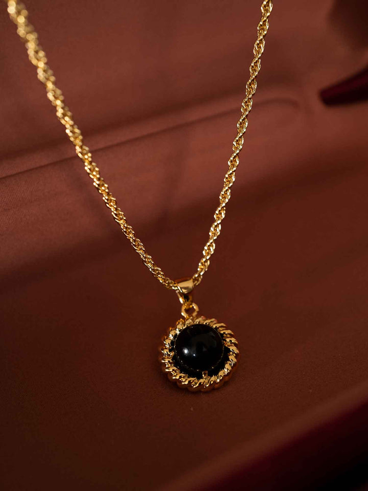 Melina black acrylic gold pendant necklace styled on brown fabric