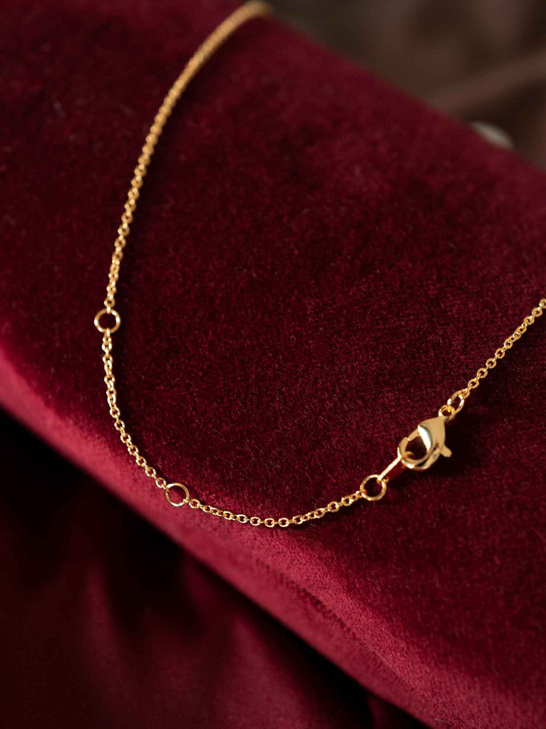 Clasp detail of Renira gold pendant necklace on red fabric