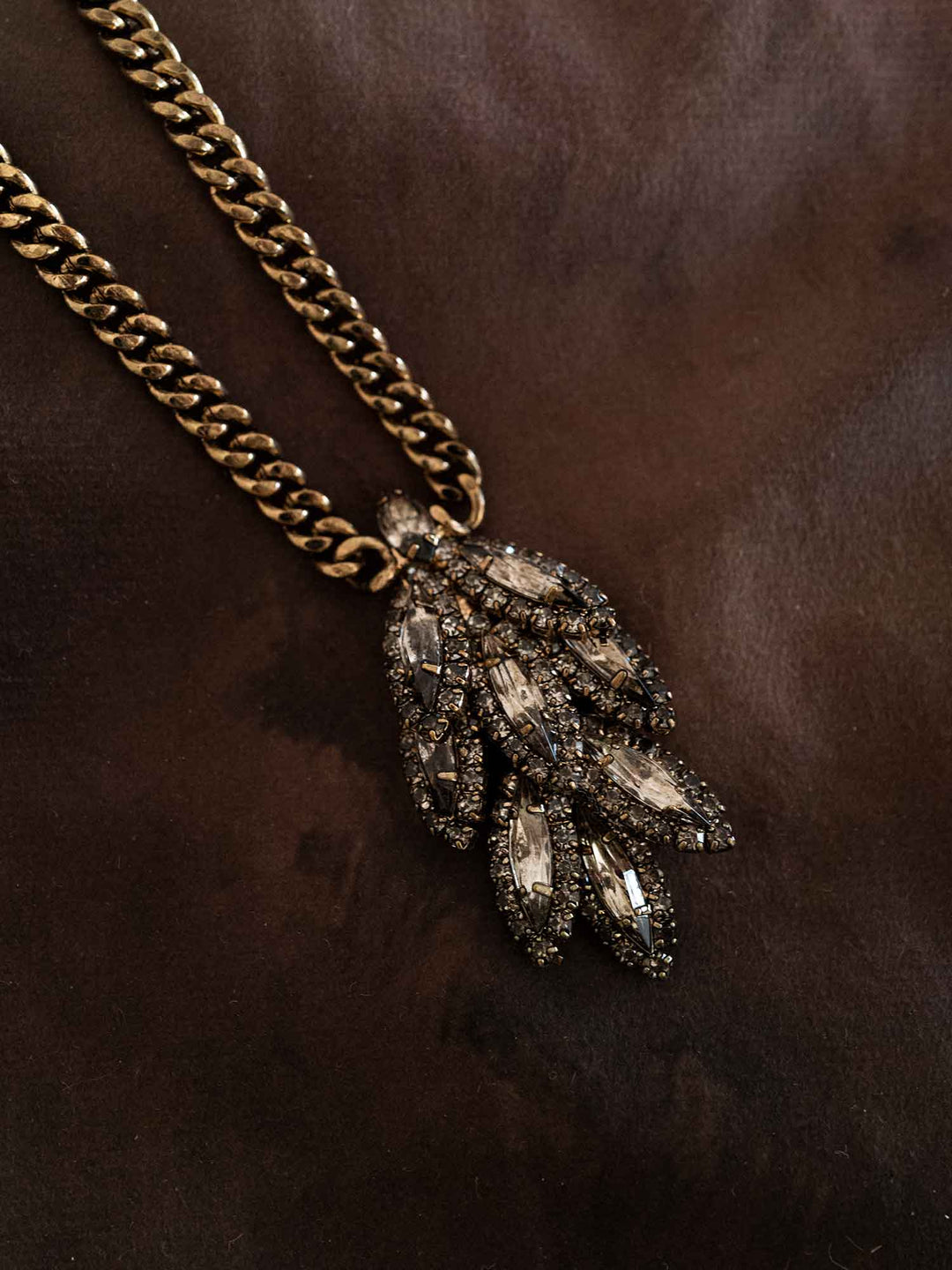 Detail view of Selene smoky crystal leaf pendant necklace styled on dark fabric