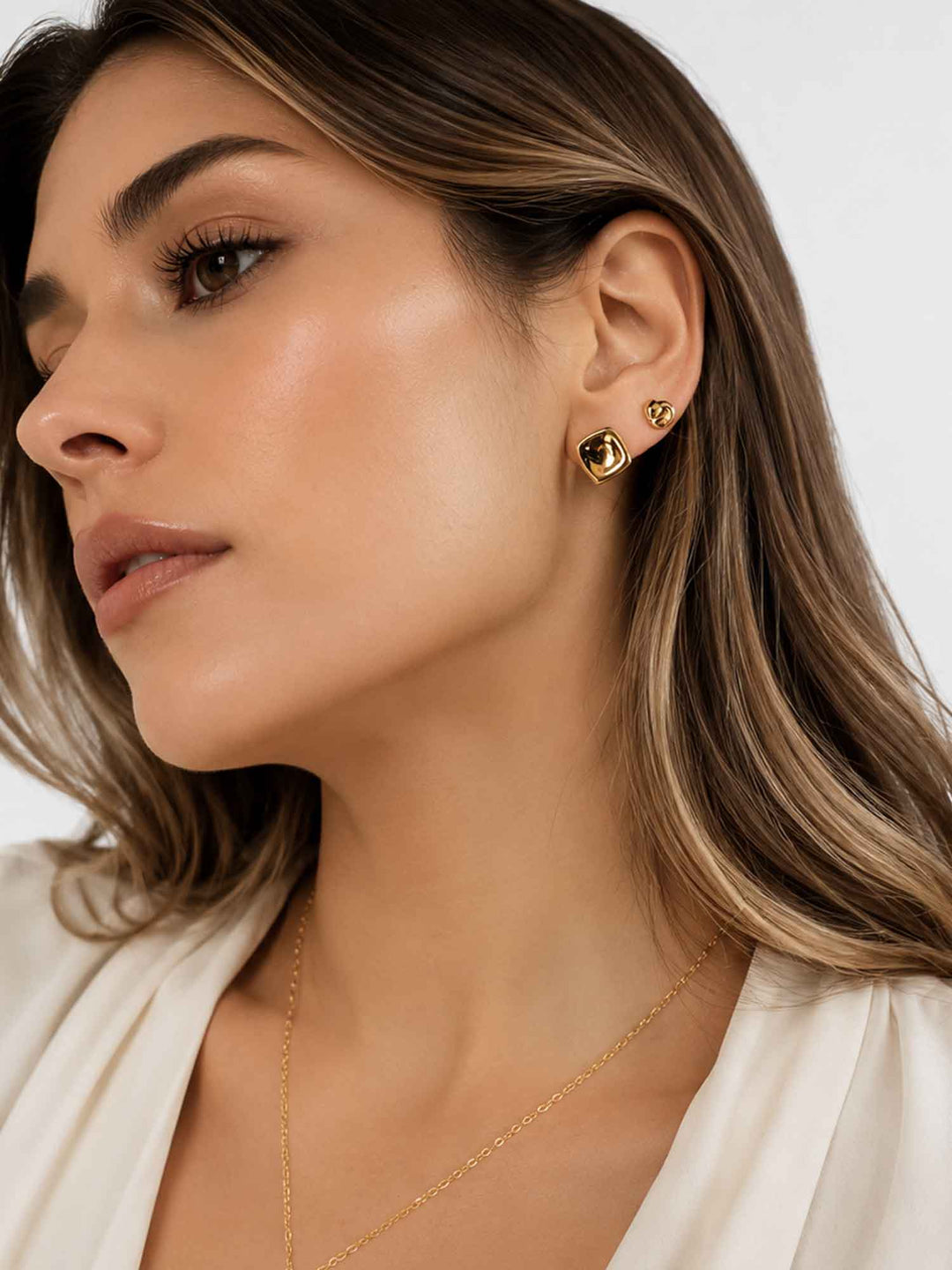 Model wearing square and knot gold cartilage earring set with white blazer