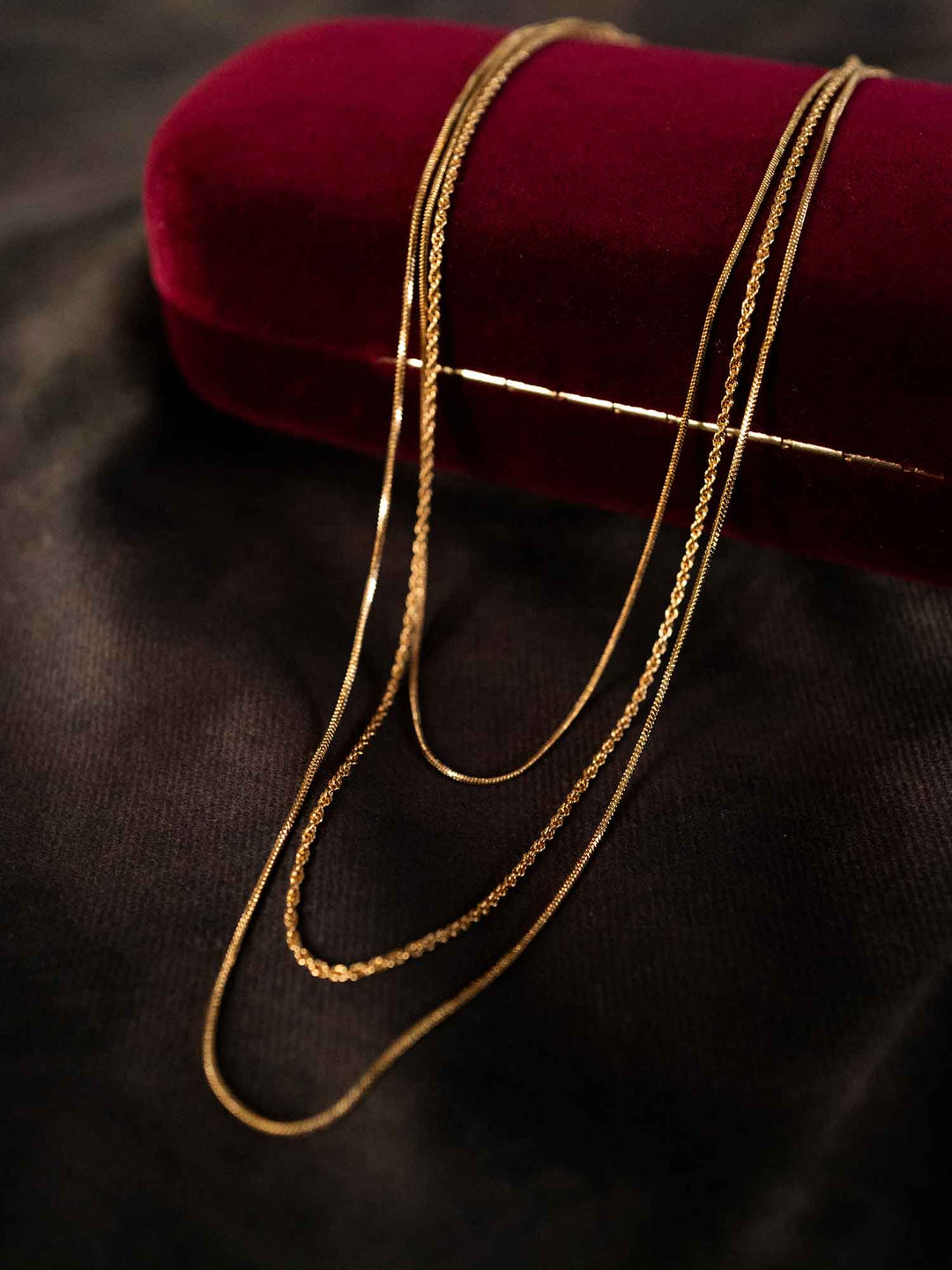Thesira layered gold chain necklace styled on red fabric