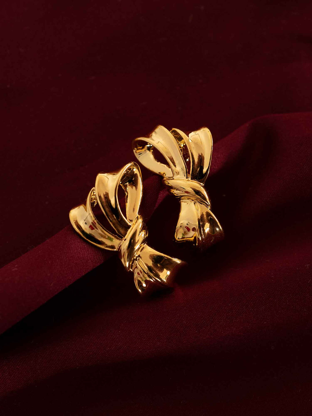 Zaya sculptural gold ribbon stud earrings styled on red fabric
