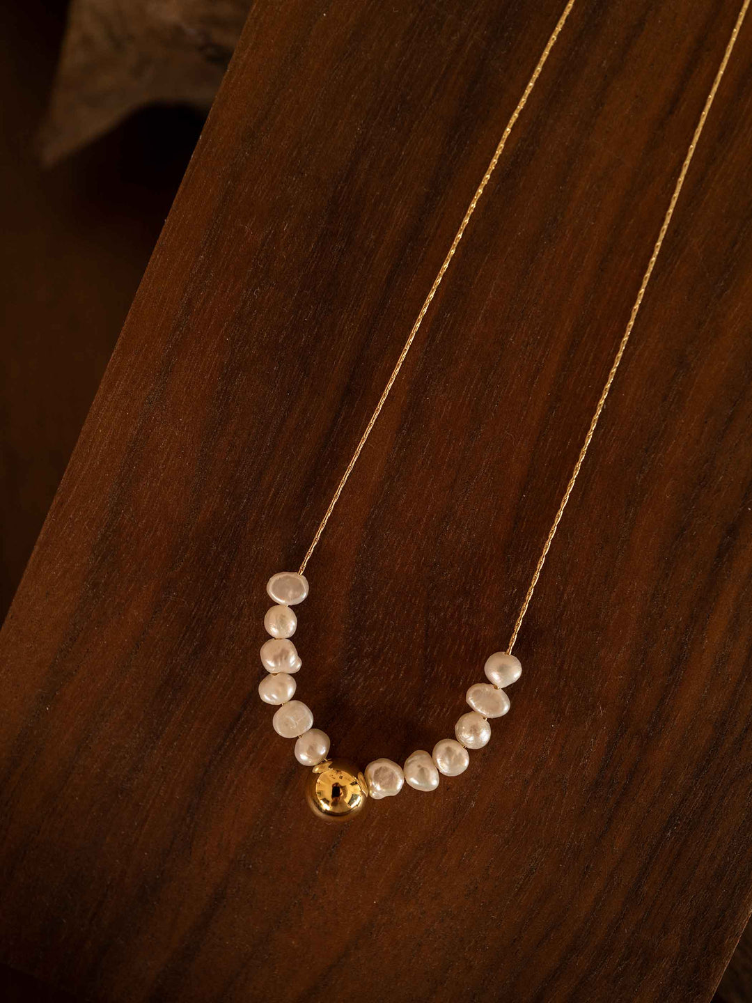 Collar de perlas de agua dulce cultivadas bañado en oro de 18K sobre una tabla de madera de tono vintage